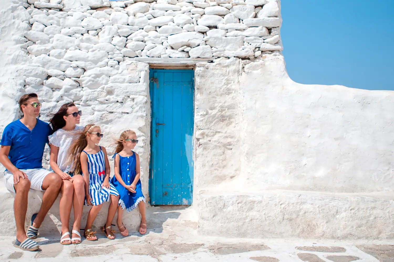 Ferry to Cyclades Islands - Family vacation in Europe. Parents and kids at street of typical greek traditional village with white walls and colorful doors on Mykonos Island, in Greece.