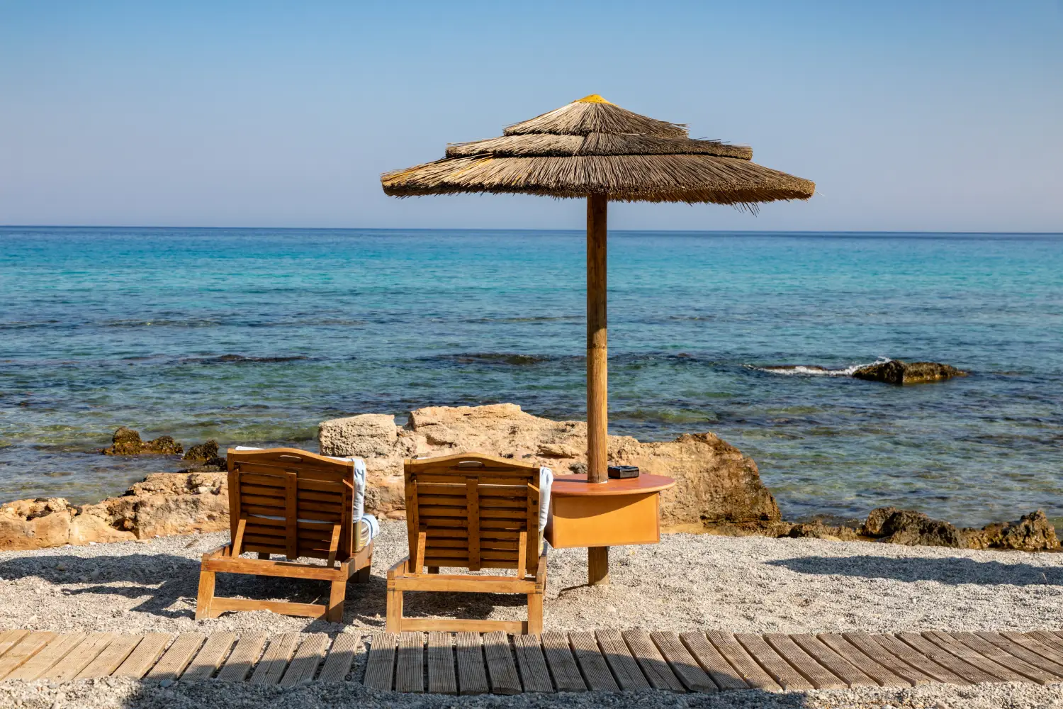 Ferry to Kamiros Skala Rhodes - Umbrella with two sun beds on the beach overlook the rocks and the sea.