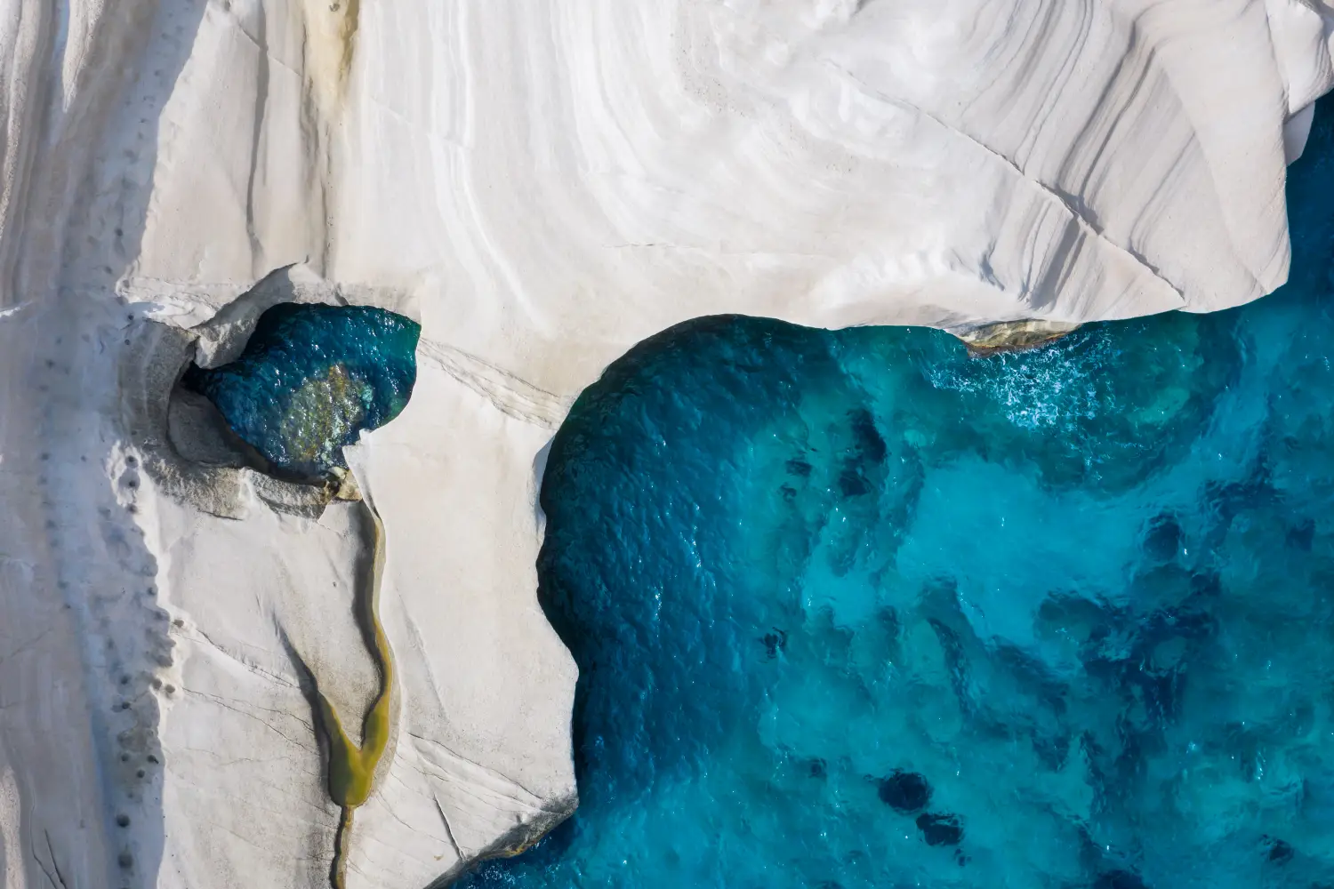 Ferry to Milos - Aerial top down view to the chalk rock formations of Sarakiniko with sparkling blue sea, Milos island, Cyclades, Greece.