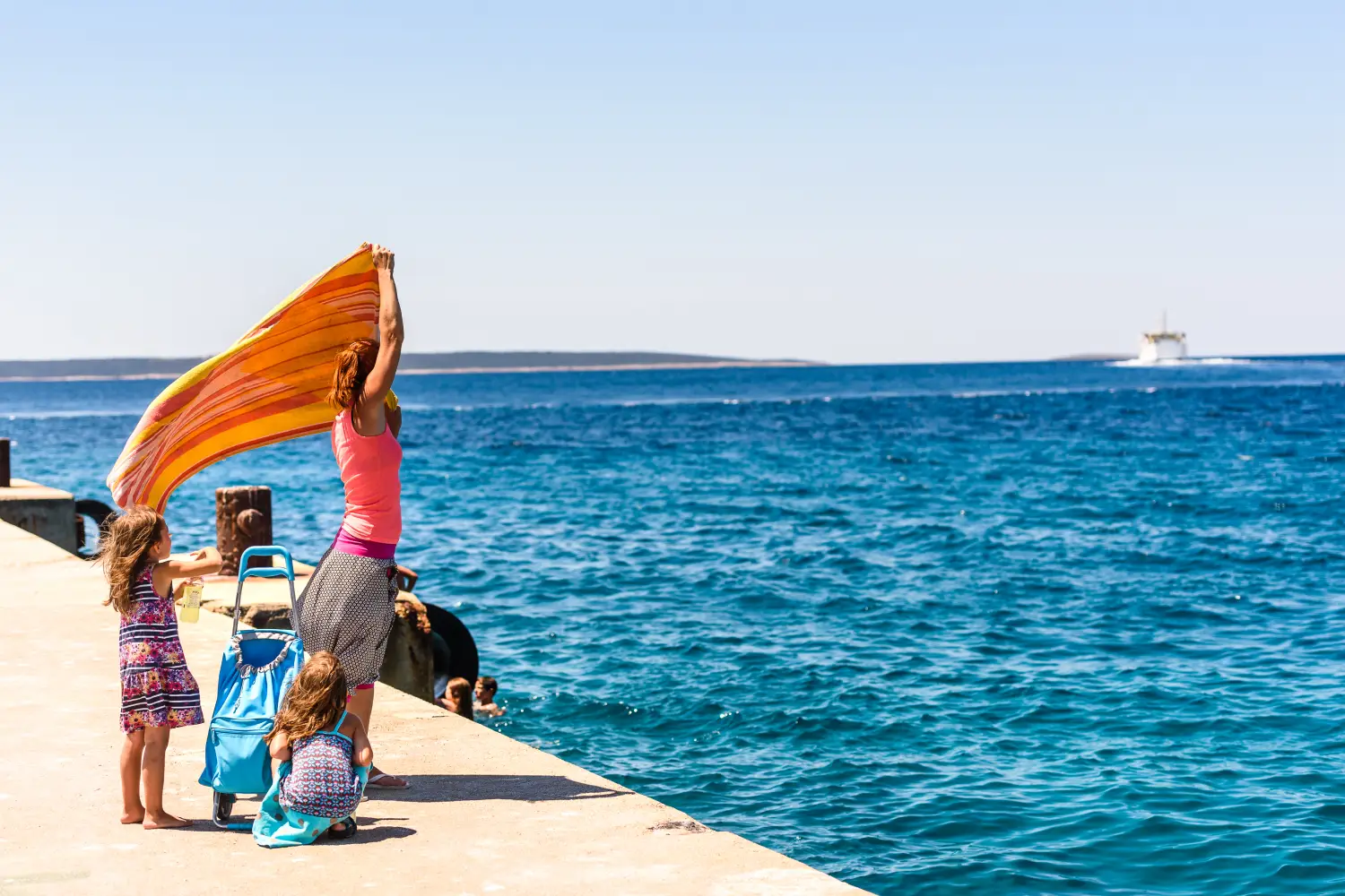 Ferry to Premuda - Mother and twin girls standing on pier with luggage in summertime waving goodbye to ferry boat leaving island Silba to island Premuda, Croatia.