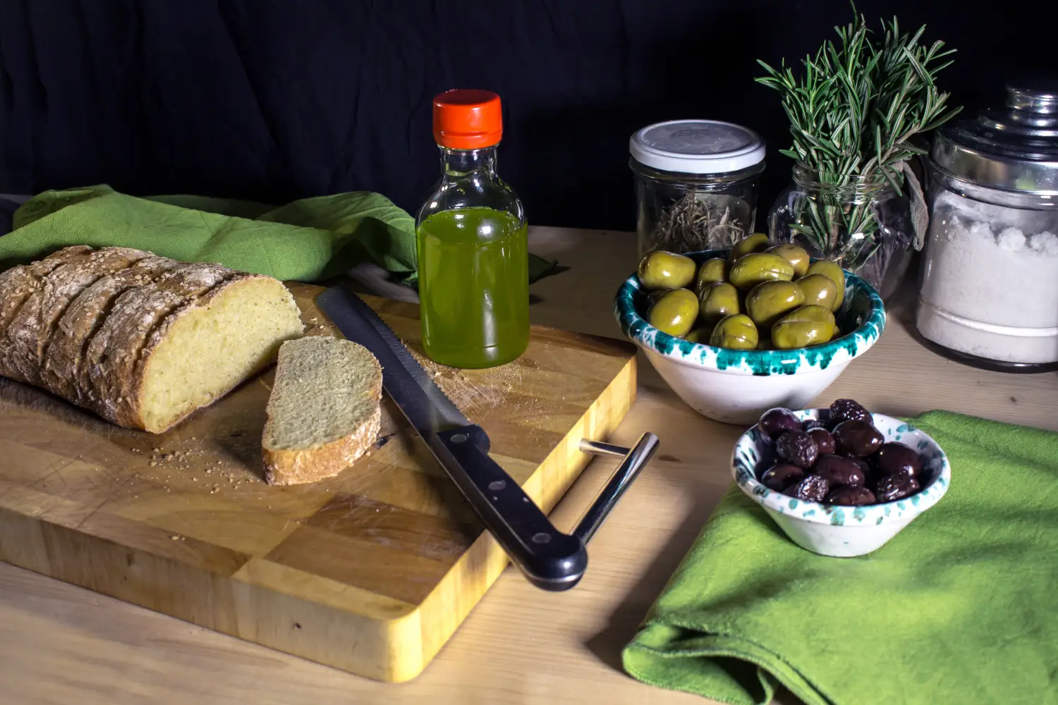 Ferry to Trapani - Still life with extra virgin olive oil from Trapani, sliced homemade bread on cutting board and containers with white and black olives.